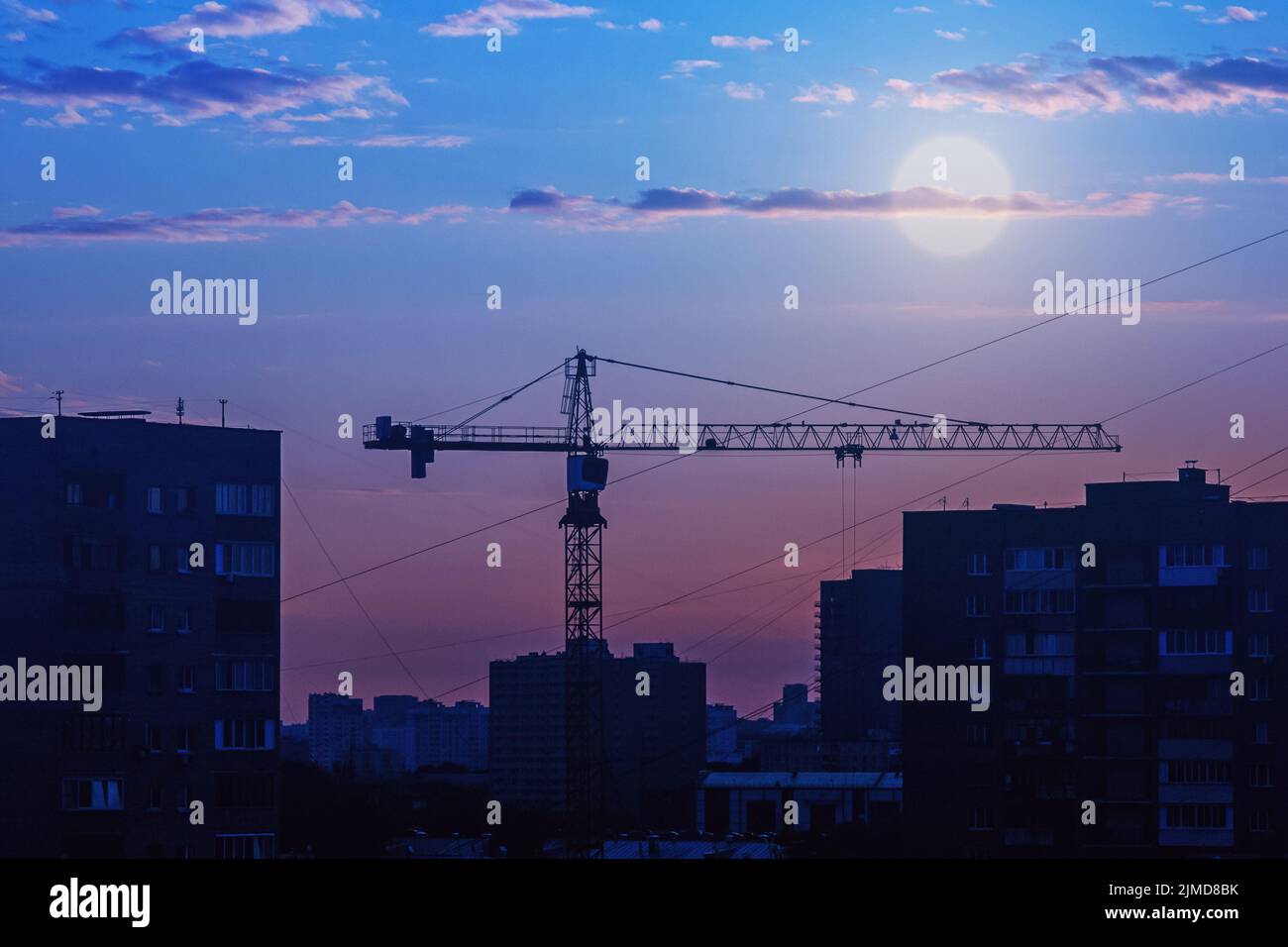 Construction crane silhouette against city skyline, full moon over night city Stock Photo