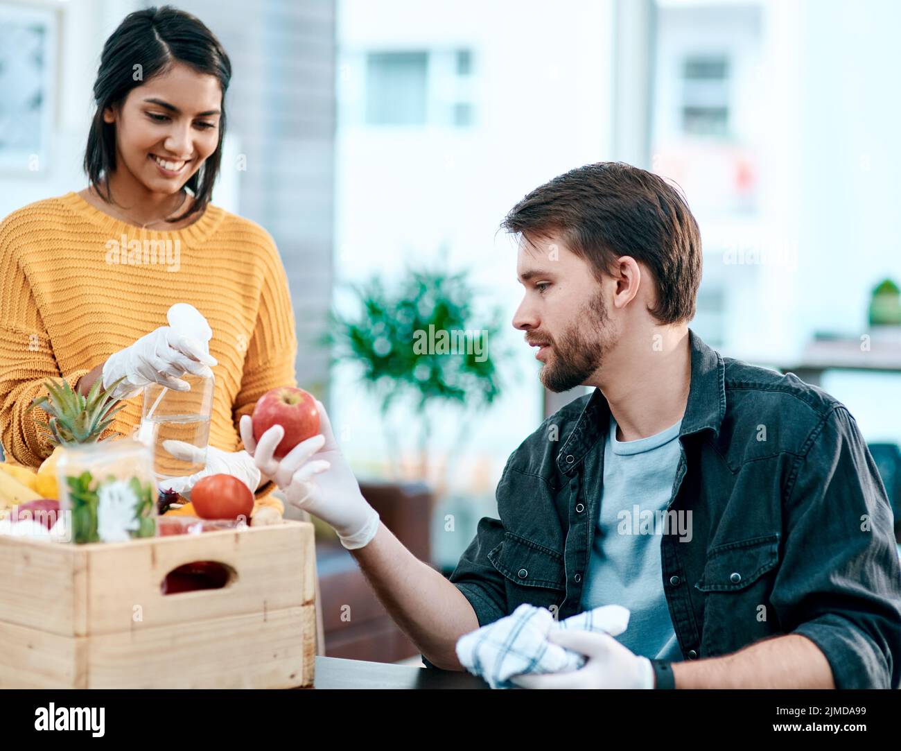 Times of crisis need extra care. a young couple disinfecting their groceries at home. Stock Photo