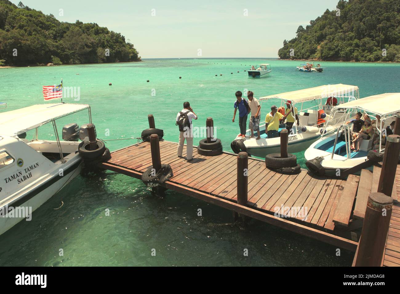 Visitors stepping out of boats as they are arriving at a jetty on Pulau Sapi (Sapi Island), a part of Tunku Abdul Rahman Park in Sabah, Malaysia. Stock Photo