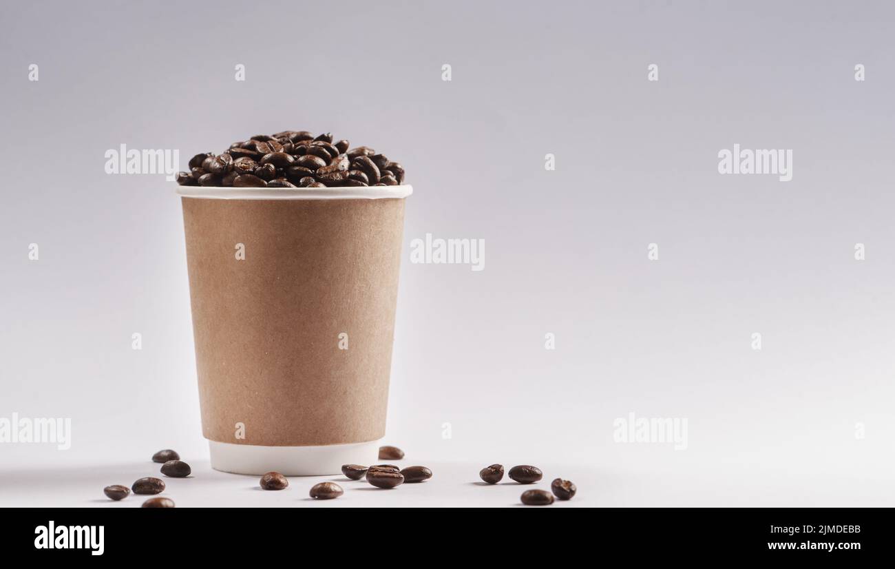 Lets meet for coffee. Studio shot of a paper cup filled with coffee beans against a grey background. Stock Photo