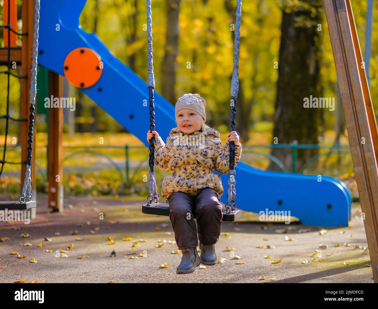 Baby girl sitting on a swing on a playground in an autumn park. Stock Photo