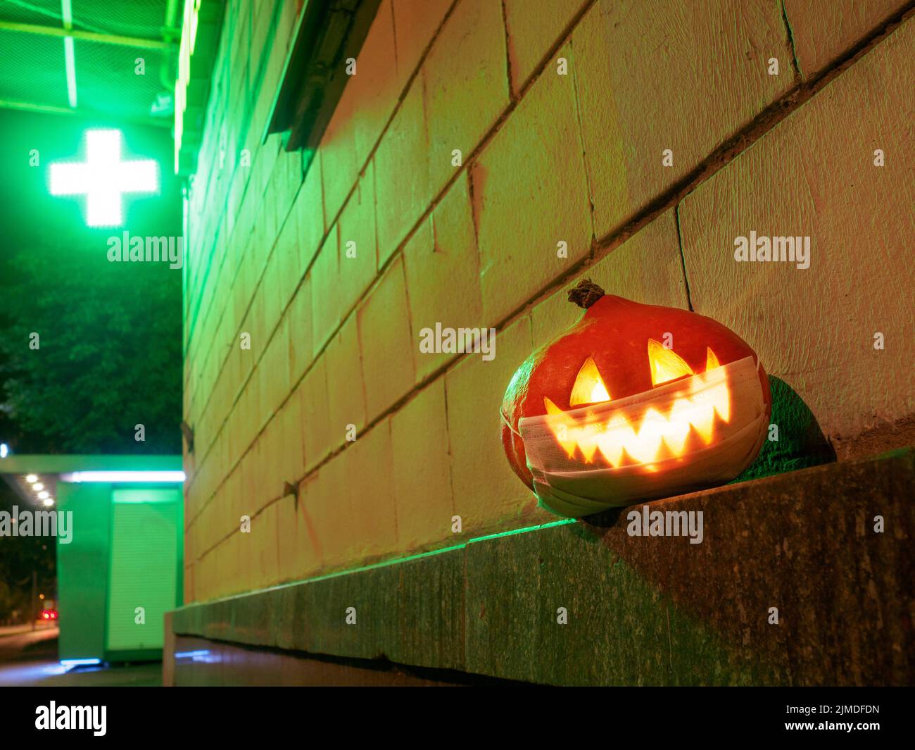 Halloween pumpkin with a protective mask on his face against the background of a pharmacy cross. Stock Photo