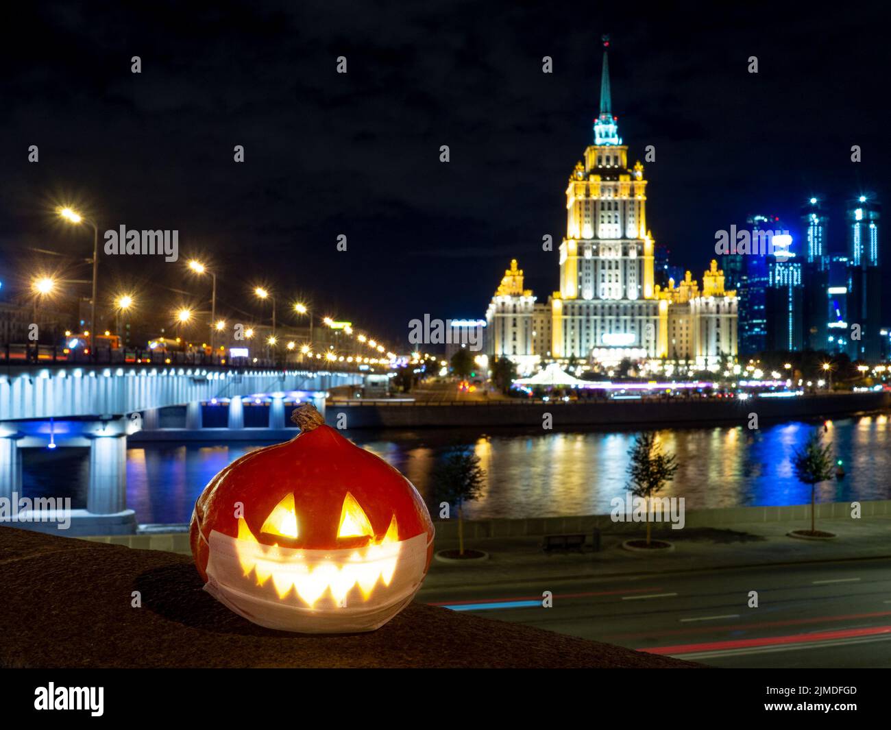 Halloween pumpkin on the background of the night city. Multi-storey buildings and skyscrapers. Blurry colored lights are reflect Stock Photo