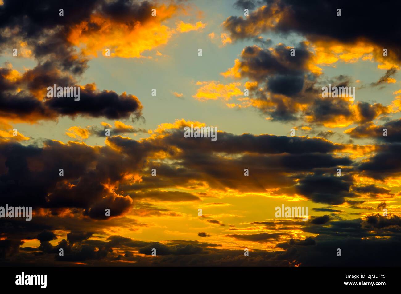 A very dramatic sky full of yellows, blues and oranges. Contrasting clouds during sunset illuminated by the setting sun. Bright Stock Photo