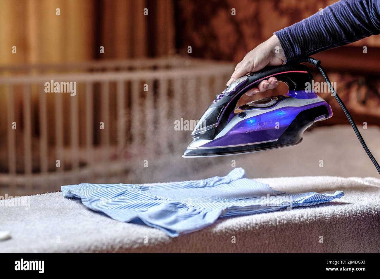 Closeup female hand ironing clothes on the table. Puffs of hot steam. Stock Photo