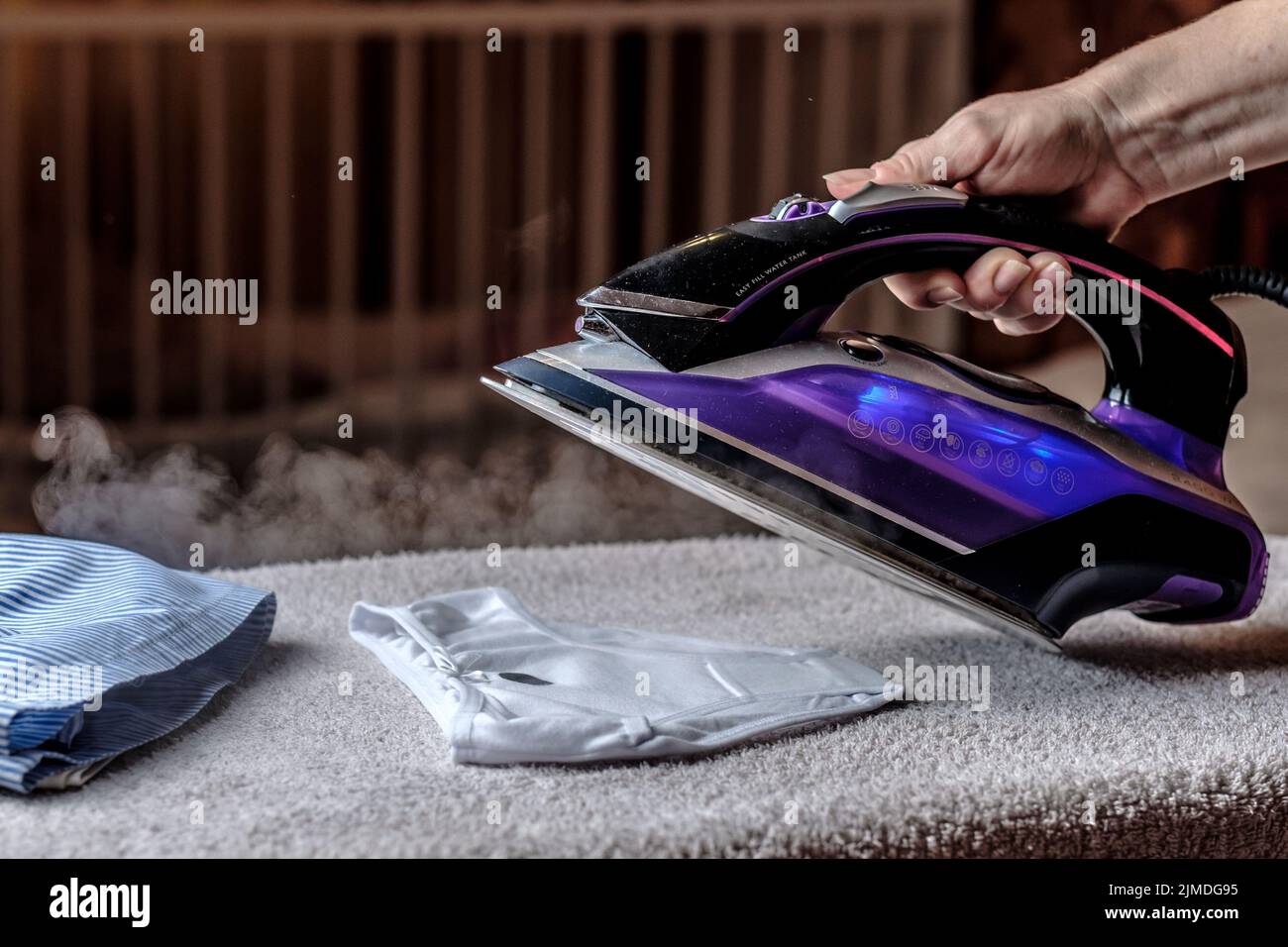 Closeup female hand ironing clothes on the table. Puffs of hot steam. Stock Photo