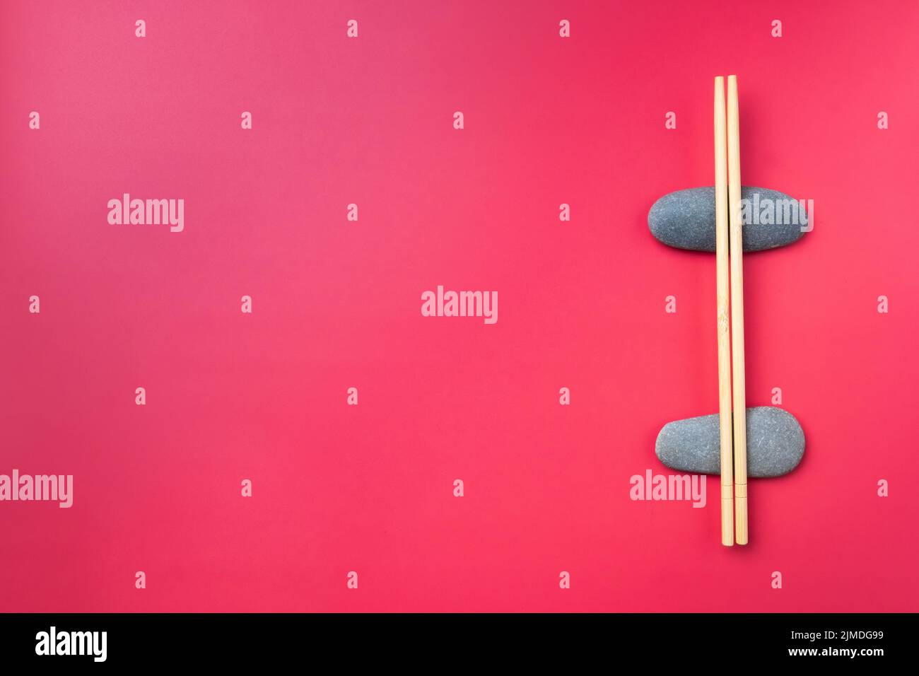 Flat lay. Light wooden chopsticks lie on oval stones on a pink background. Stock Photo
