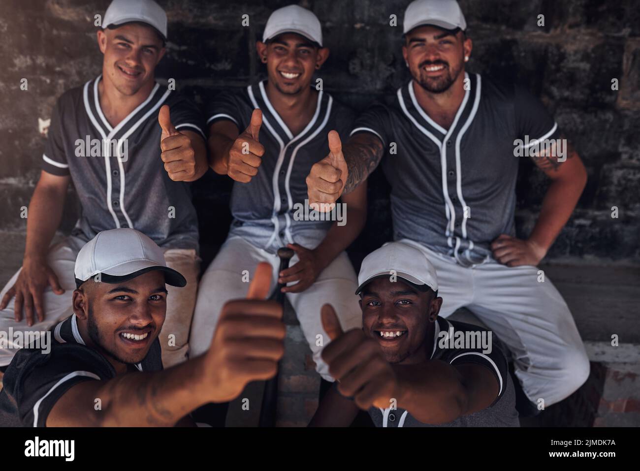 Good game. a group of young baseball players sitting in the dugout and showing thumbs up. Stock Photo