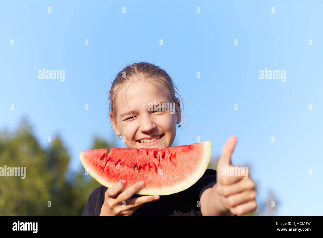 Cheerful charming teen girlfriend showing you thumb up while holding watermelon slice Stock Photo