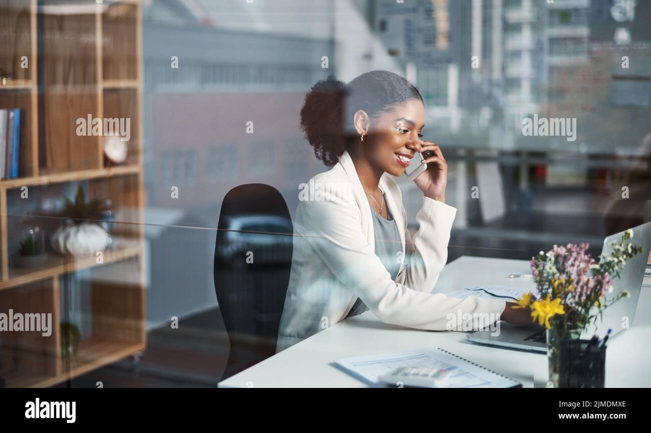 Business woman on a phone call sitting at a desk typing an email on a office computer. Smiling corporate female talking about work while working Stock Photo