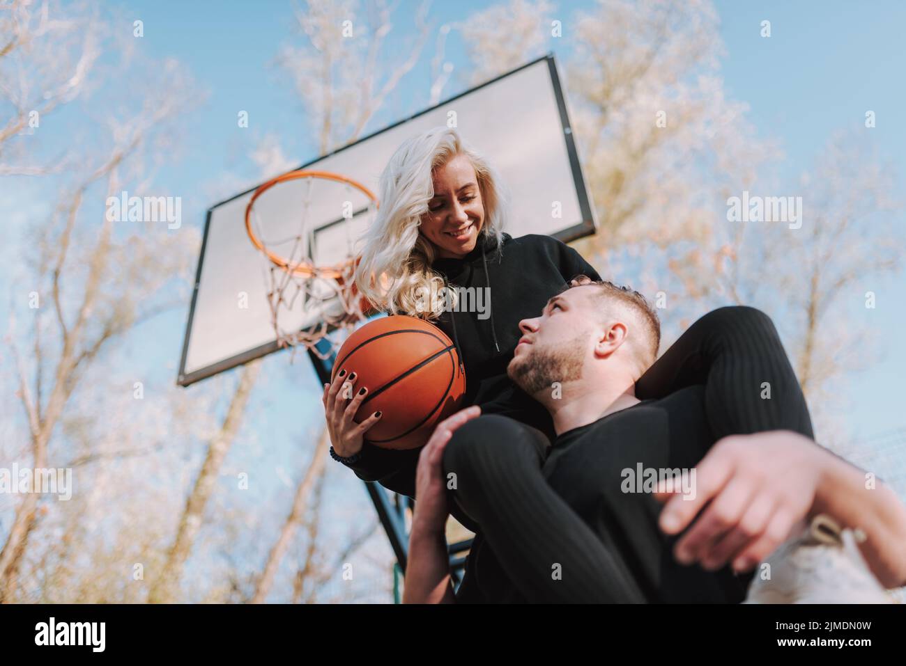 Smiling lady holding basketball ball and looking at guy Stock Photo