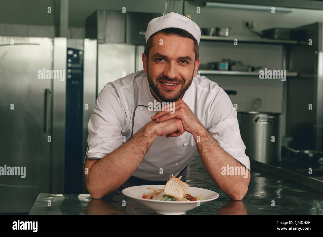 Portrait of smiling chef in uniform with cesar salat on modern kitchen of restaurant Stock Photo