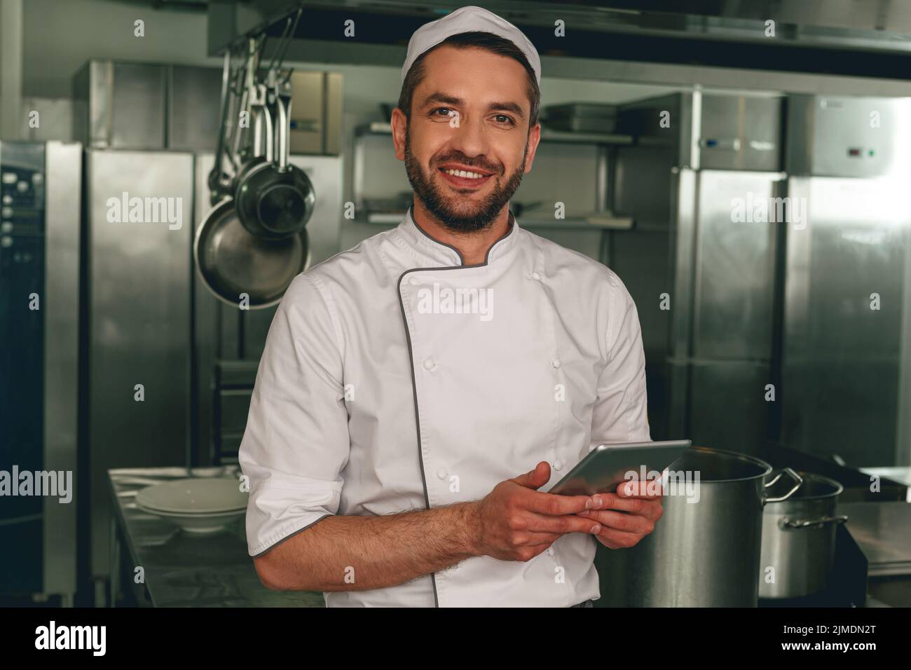 Smiling chef in uniform making order in digital tablet for the supplier standing on kitchen Stock Photo