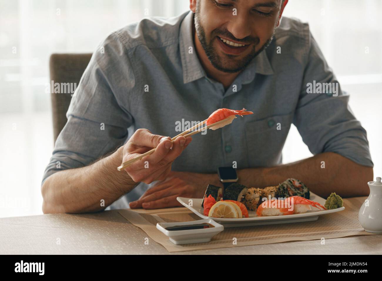 Happy man holding chopsticks with tasty sushi in japanese restaurant Stock Photo