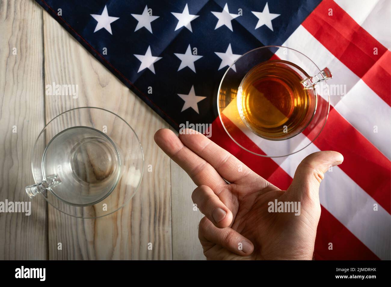 Table separated by American flag with full cup and empty cup on table and man's hand in V position Stock Photo