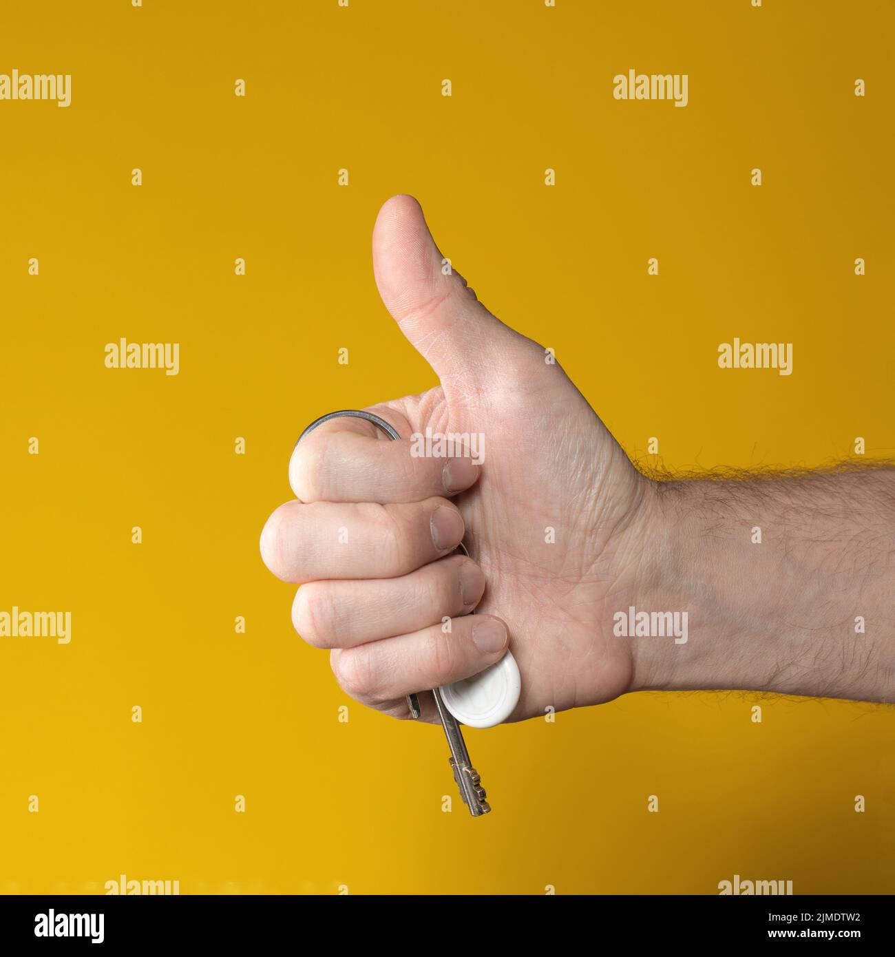 Man hand holding house keys on yellow background. makes thumbs up gesture Stock Photo