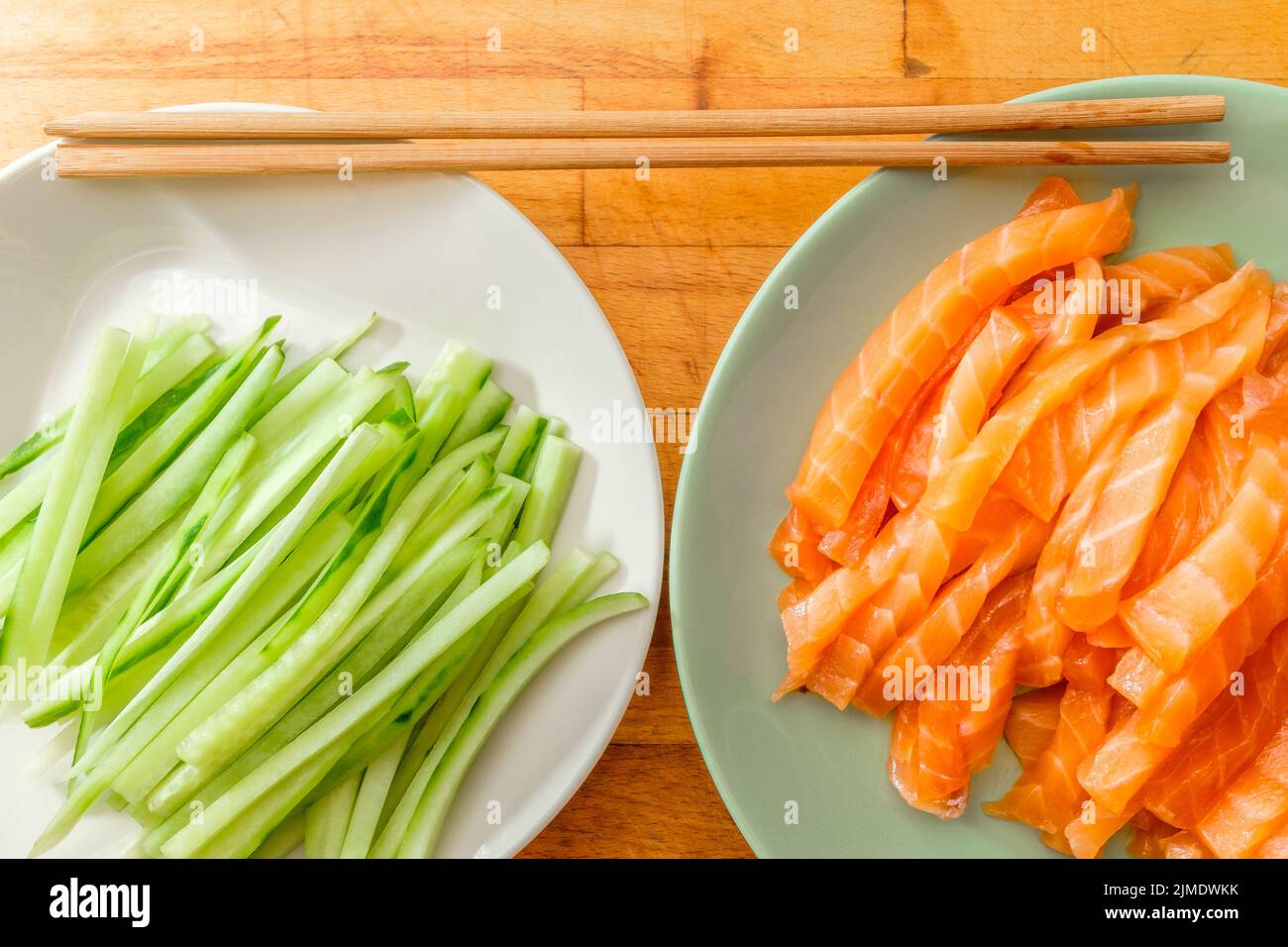 Top view of salmon and fresh cucumber slices on plates and bamboo chopsticks. Stock Photo