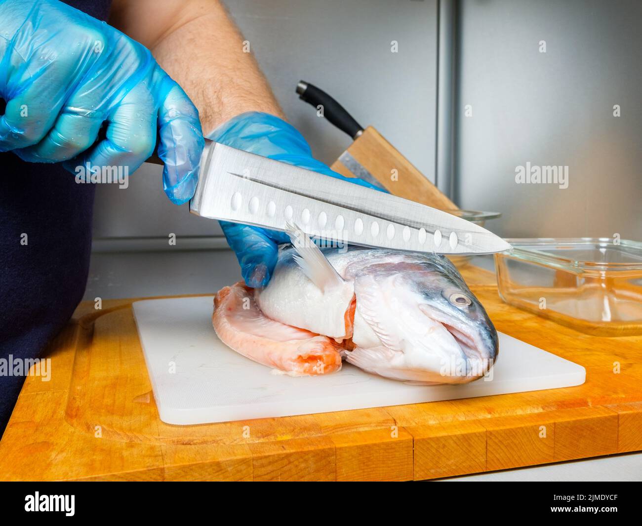 The gloved hands of the cook cut off the salmon's head with a knife. Stock Photo
