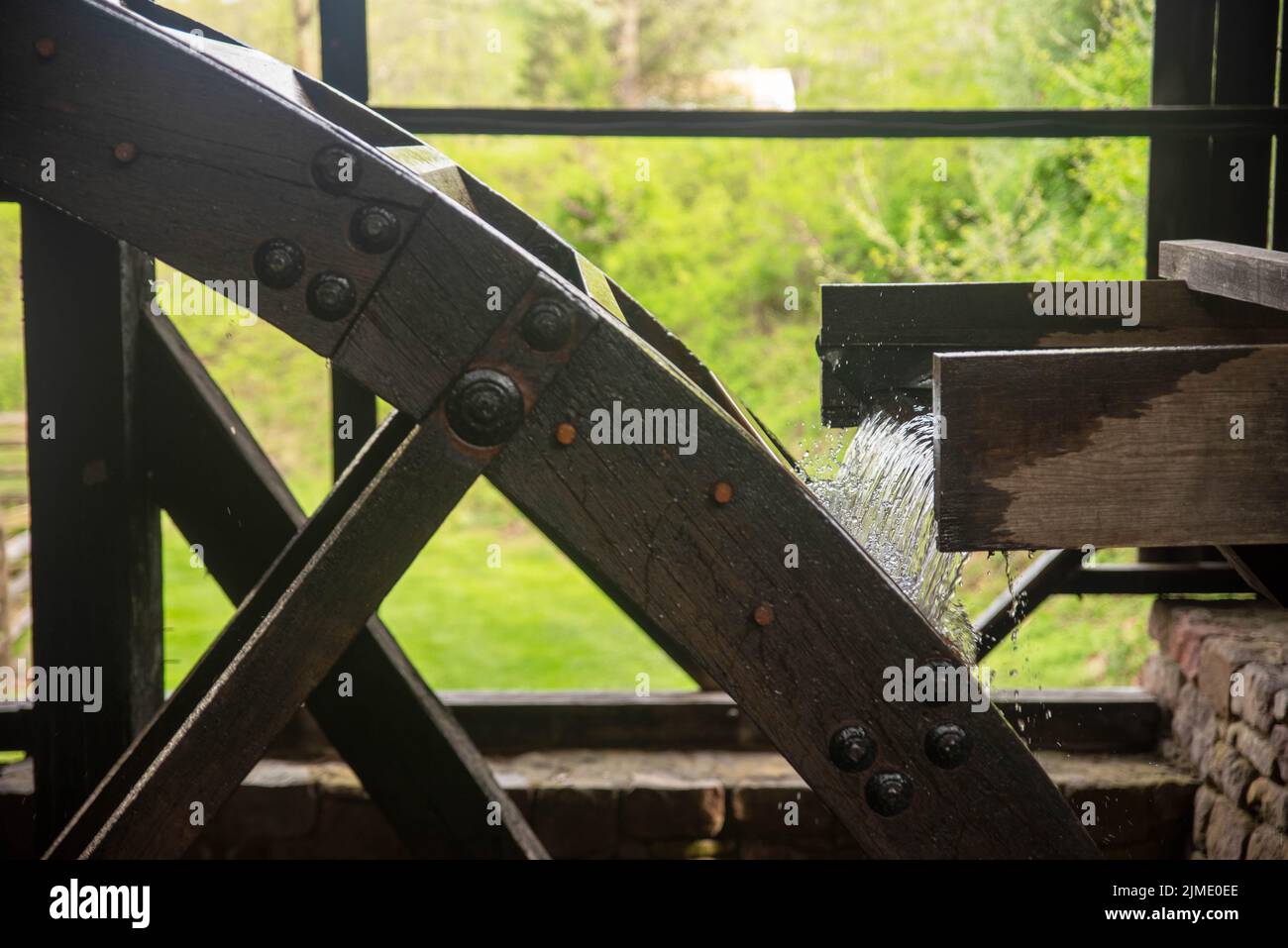 Water flows from a wooden sleuce into a hefty water wheel. Stock Photo
