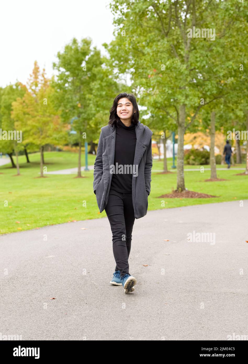 Smiling teen girl in gray jacket walking along path through park Stock Photo