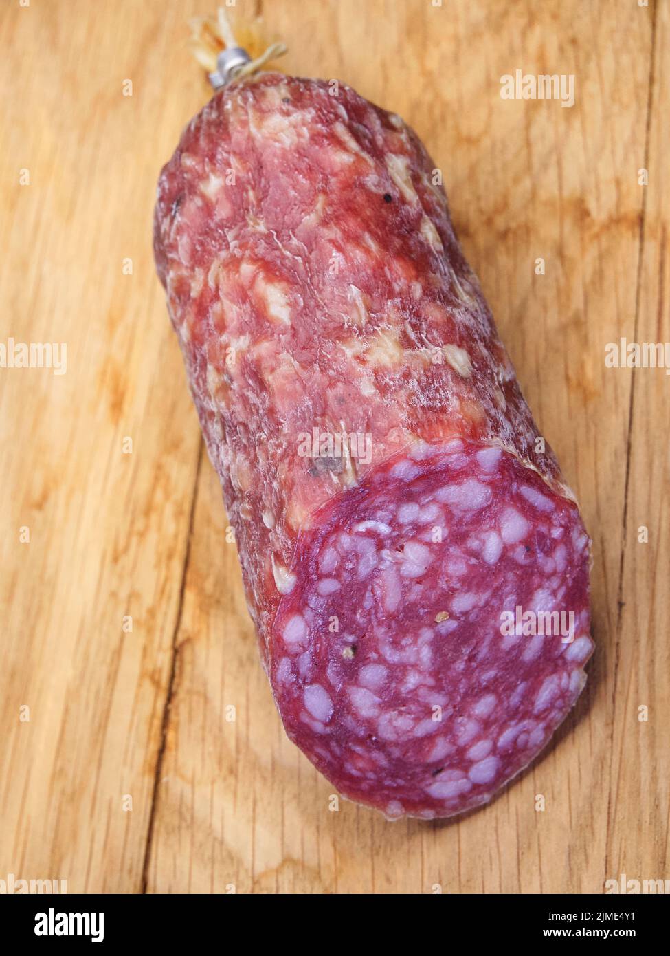 Half a stick of smoked sausage on a wooden surface. A close-up picture. Stock Photo