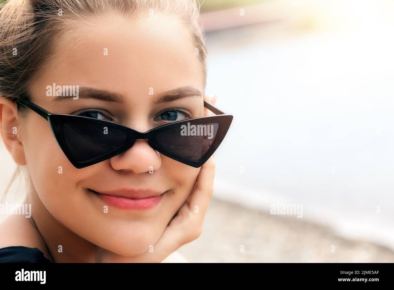 Portrait of a beautiful girl in darkened sunglasses. The look of a young Caucasian beauty from under glasses and a smile Stock Photo