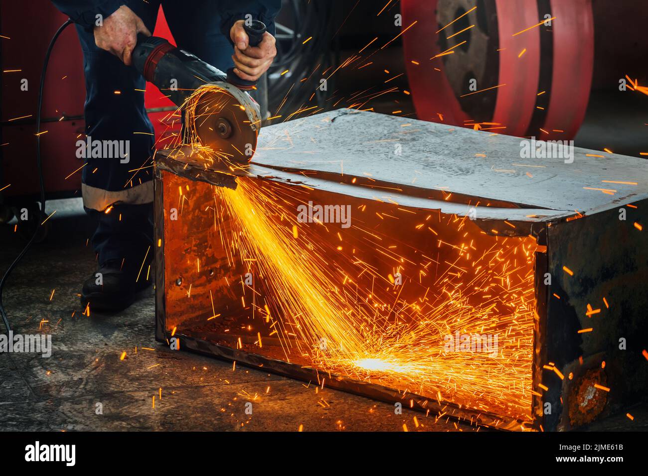 A worker cuts metal with a hand grinder in the production shop and bright sparks fly. A genuine working environment. Stock Photo