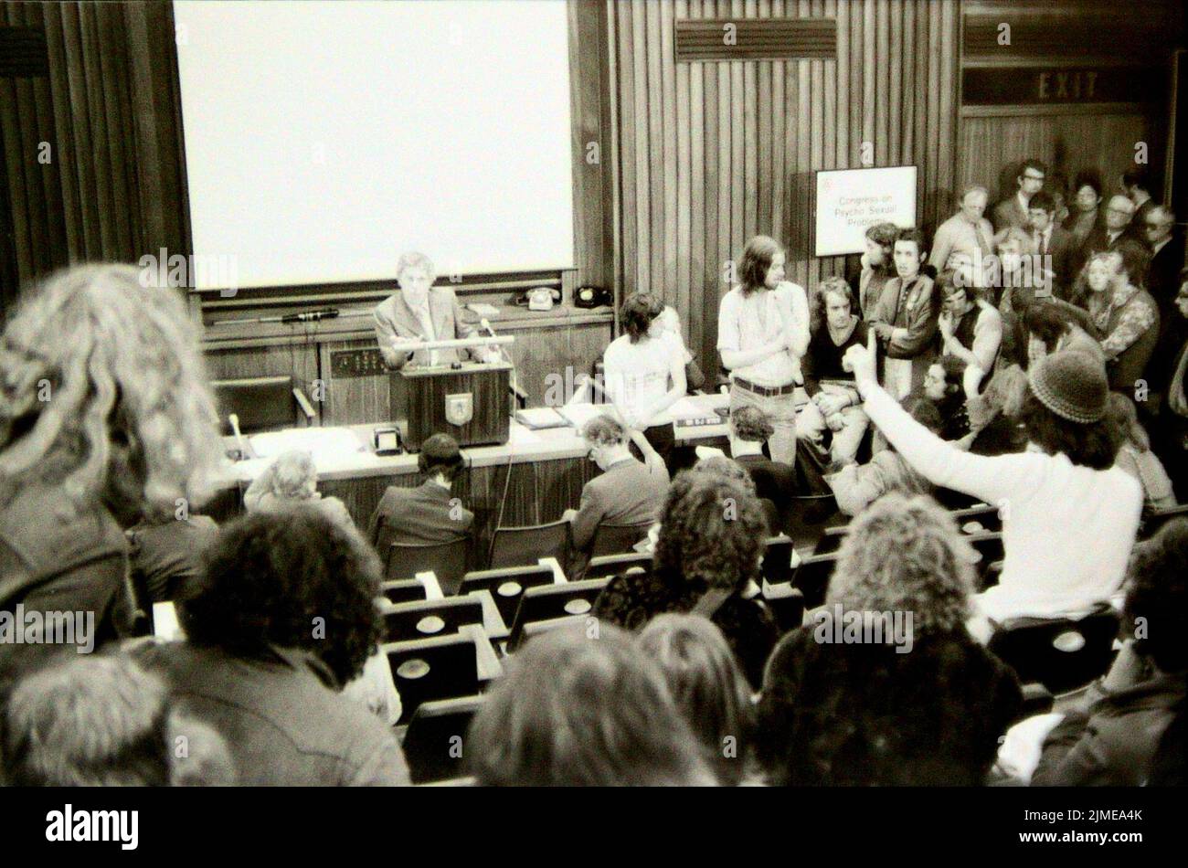 In September, 1974, dozens of lesbian and gay demonstrators entered the British Medical Association's 'Congress on Psycho-sexual Problems' in Bradford, Yorkshire, United Kingdom. The demonstrators demanded a discussion on why the medical profession viewed lesbians and gay men negatively and why 'aversion therapy' in the form of electric shocks was still used to attempt to make lesbians and gay men heterosexual. Pictured are some of the demonstrators debating with attendees of the Congress. An organiser of the Congress is at the podium. Stock Photo
