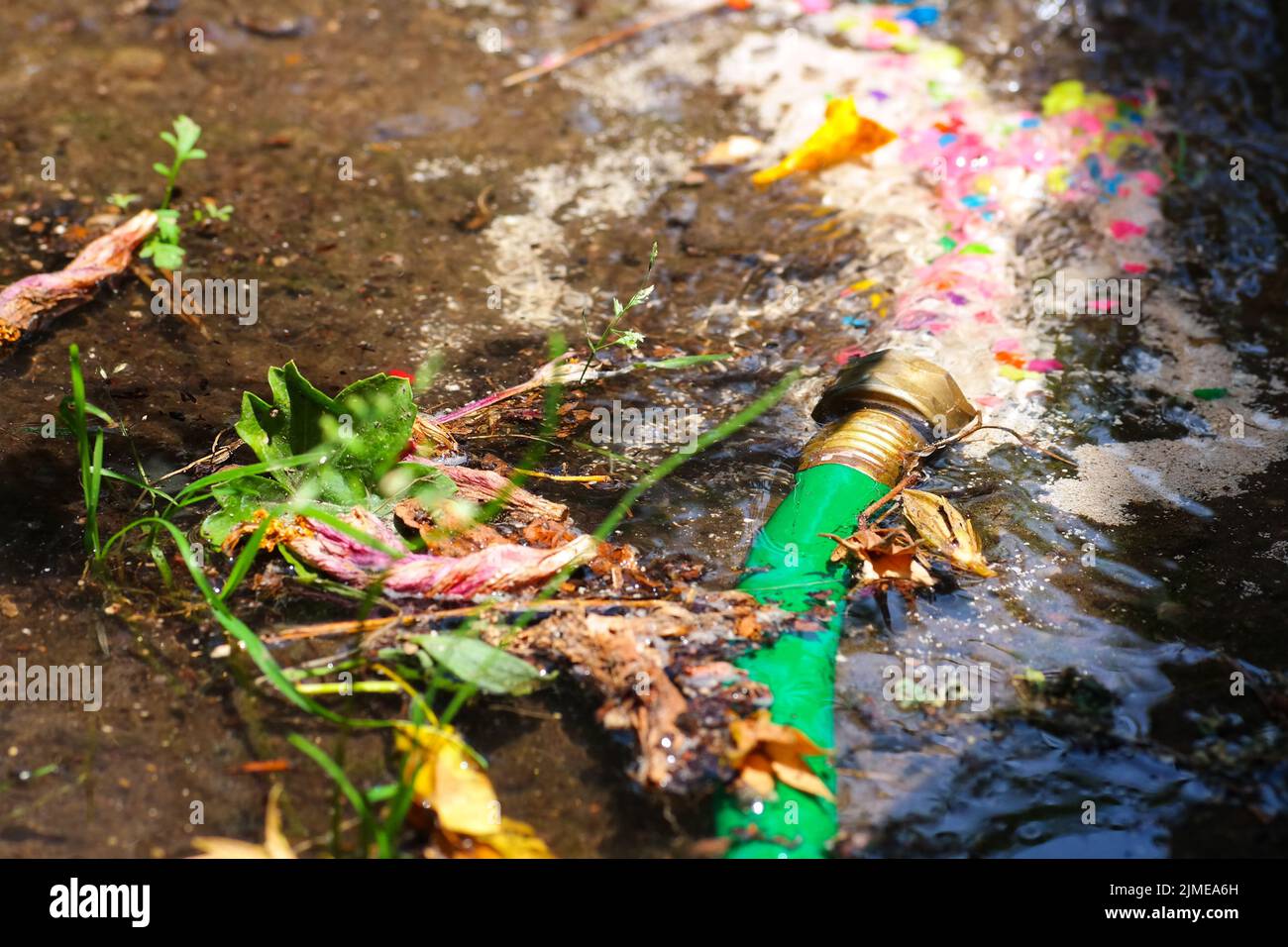 A closeup of a green water pipe splashing water under sunlight Stock
