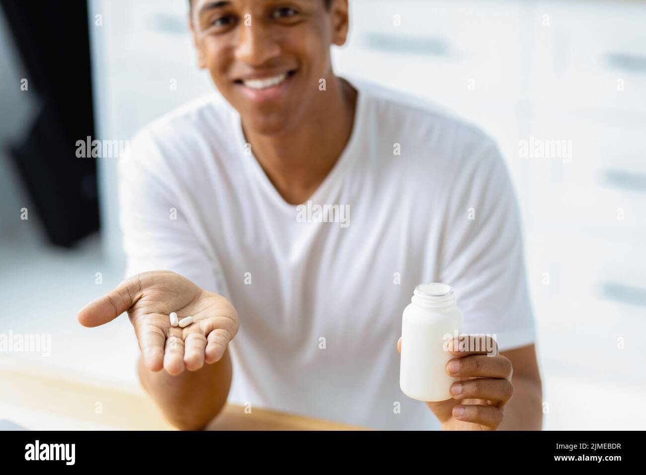 Happy young african american man holding capsules and open bottle Painkiller headache medication or vitamins Stock Photo