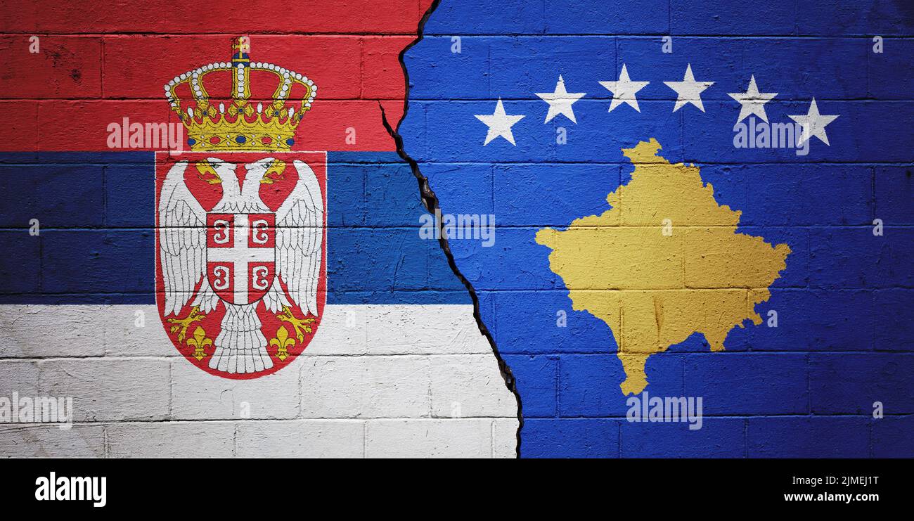 Cracked brick wall painted with a flag of Serbia on the left and a flag of Kosovo on the right. Stock Photo