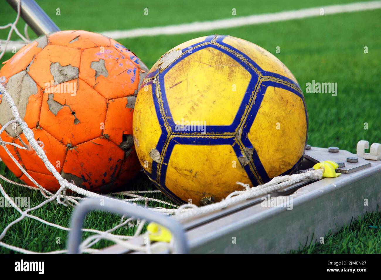 Two ragged soccer balls lying in the corner of the goal against green football field Stock Photo