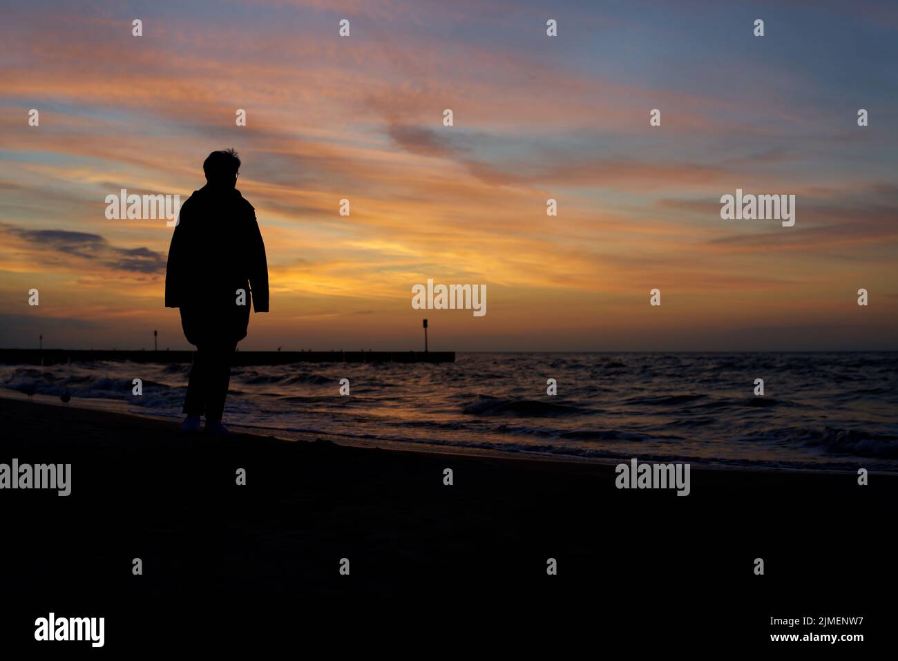 Silhouette of a vacationer walking on the beach in Kolobrzeg on the Polish Baltic coast after sunset Stock Photo