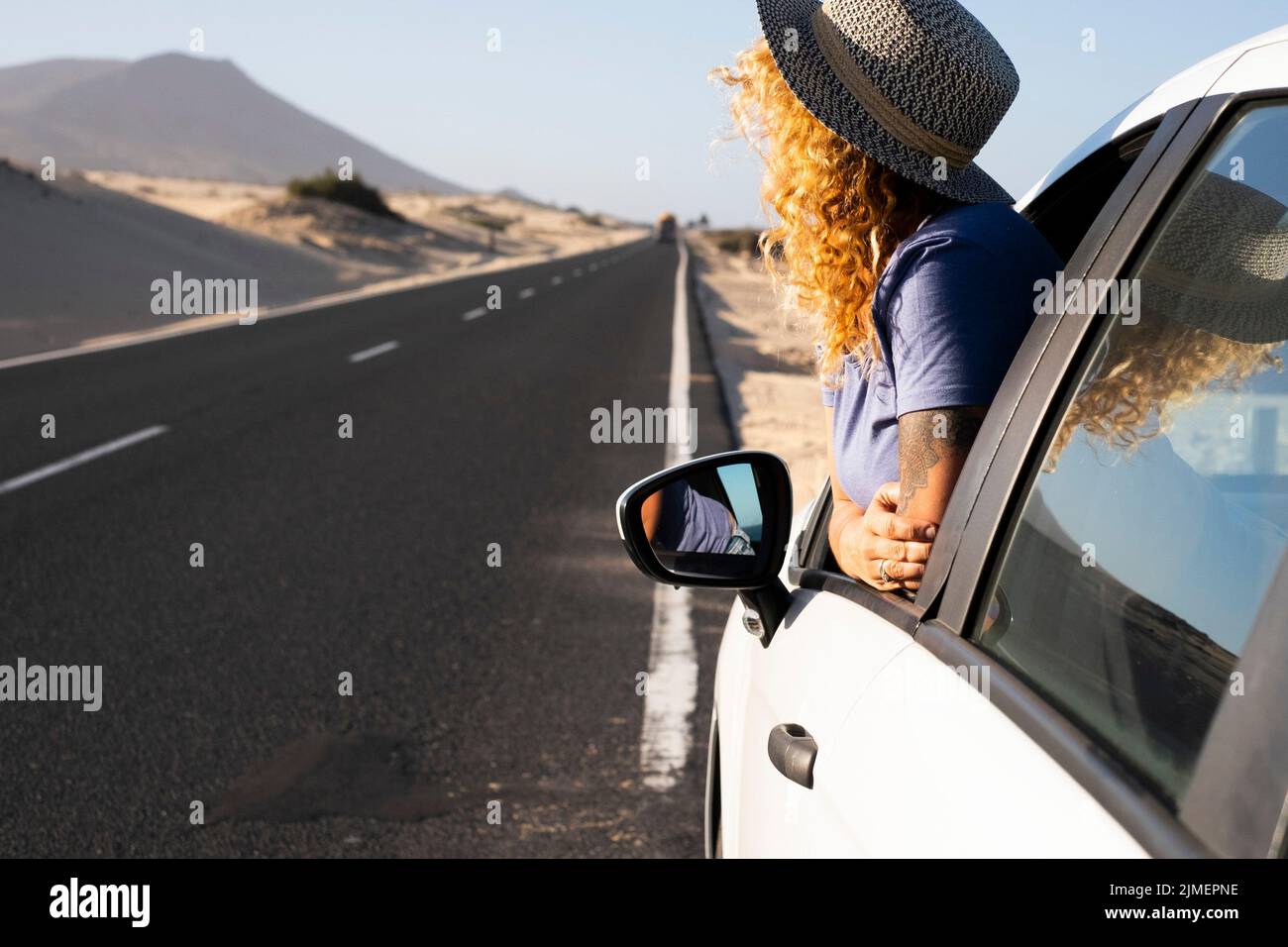 Woman enjoying road trip travel with car staying outside the window and admiring desert landscape outdoor. Traveler people for summer holiday vacation Stock Photo
