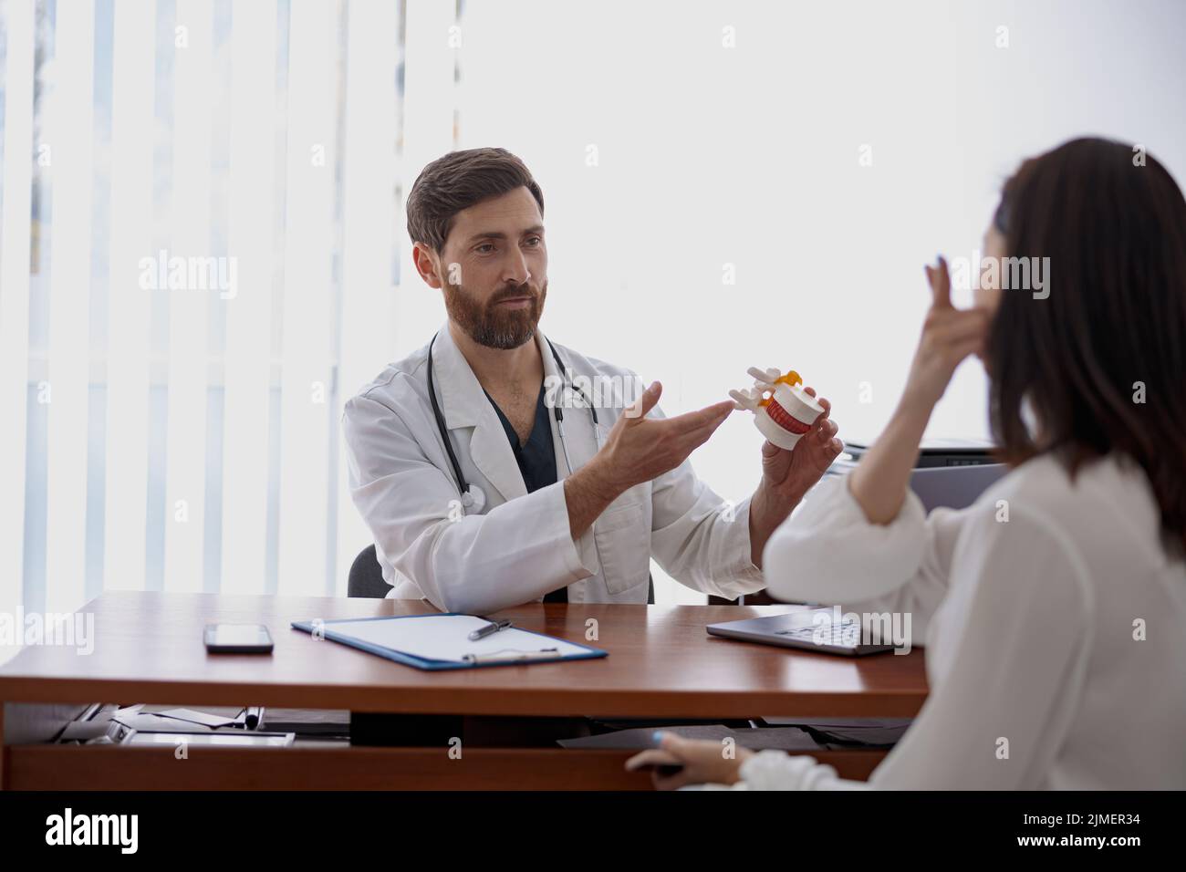 Male professional doctor consults patient and shows the model of several spines in modern clinic Stock Photo