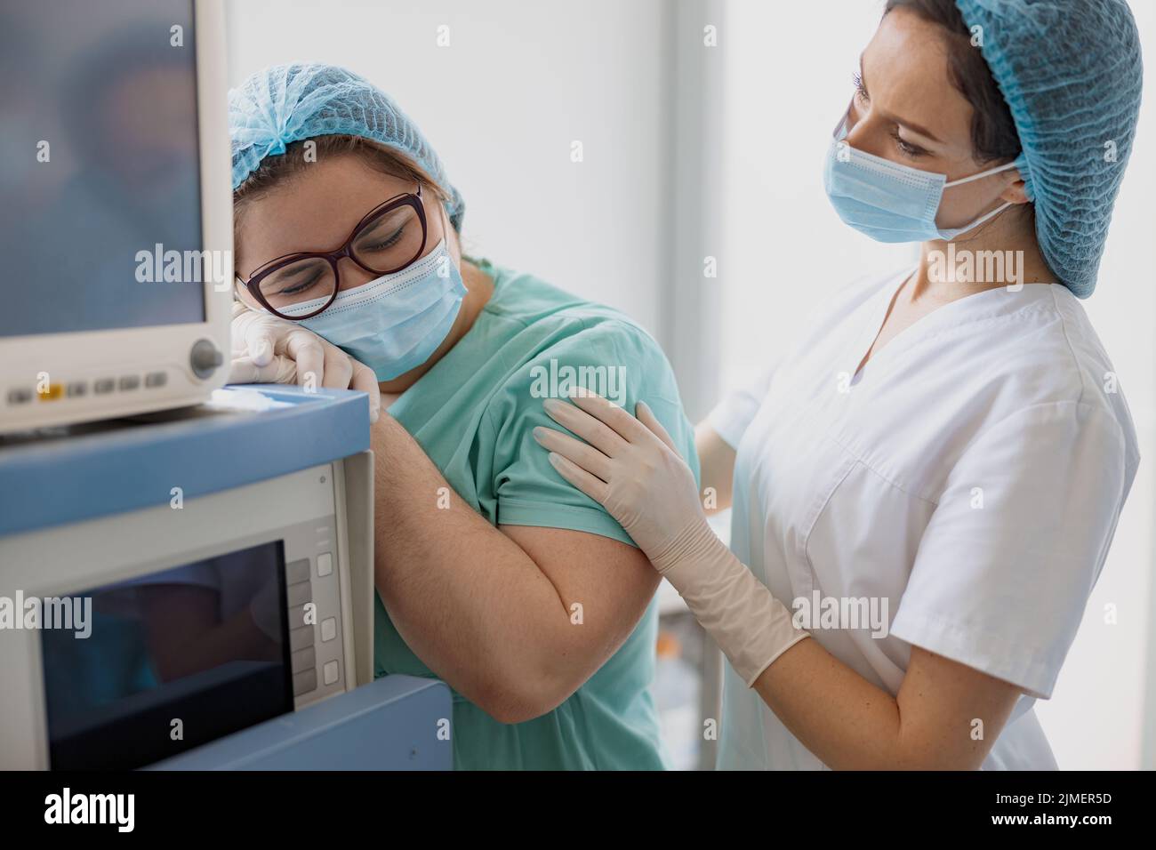 Tired nurses after difficult operation support each other in operating room Stock Photo