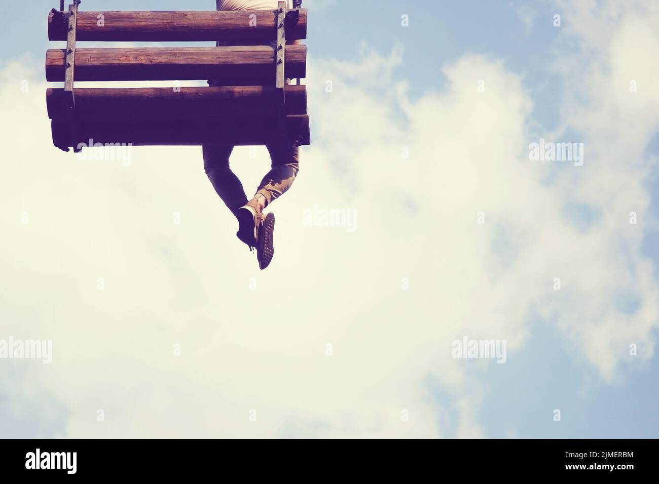 One young man sitting on wooden swing in the sky with his legs crossed