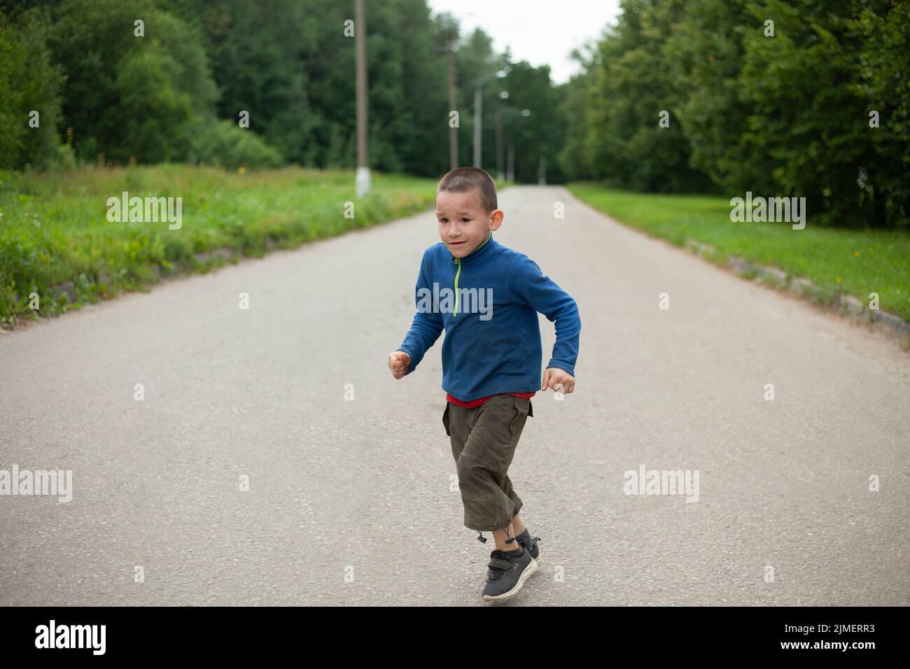 Child runs down road. Boy in summer. Schoolboy on street. Street boy in town. Stock Photo