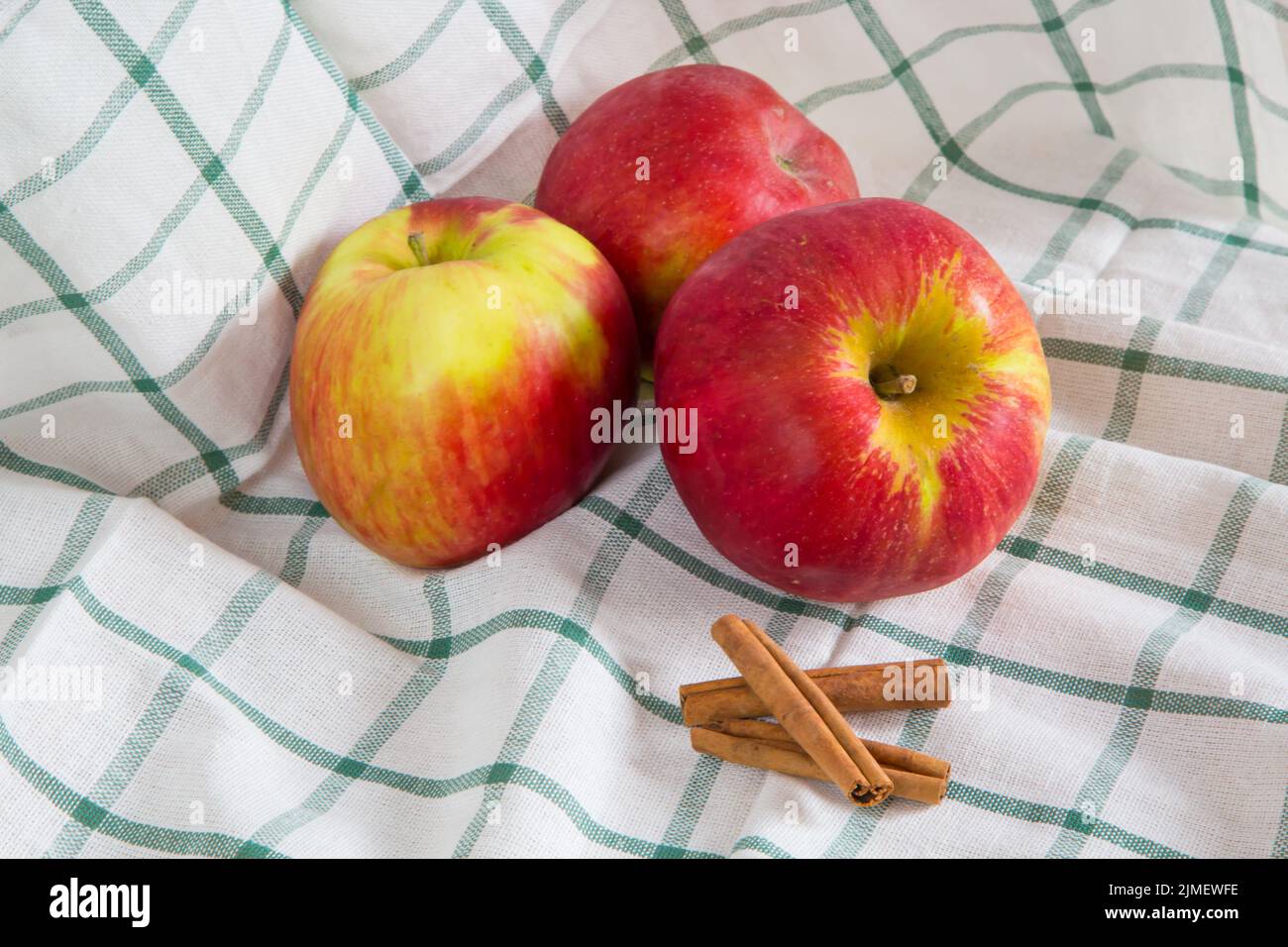 Vibrant color still life with three ripe red apples and cinnamon sticks on the cloth Stock Photo