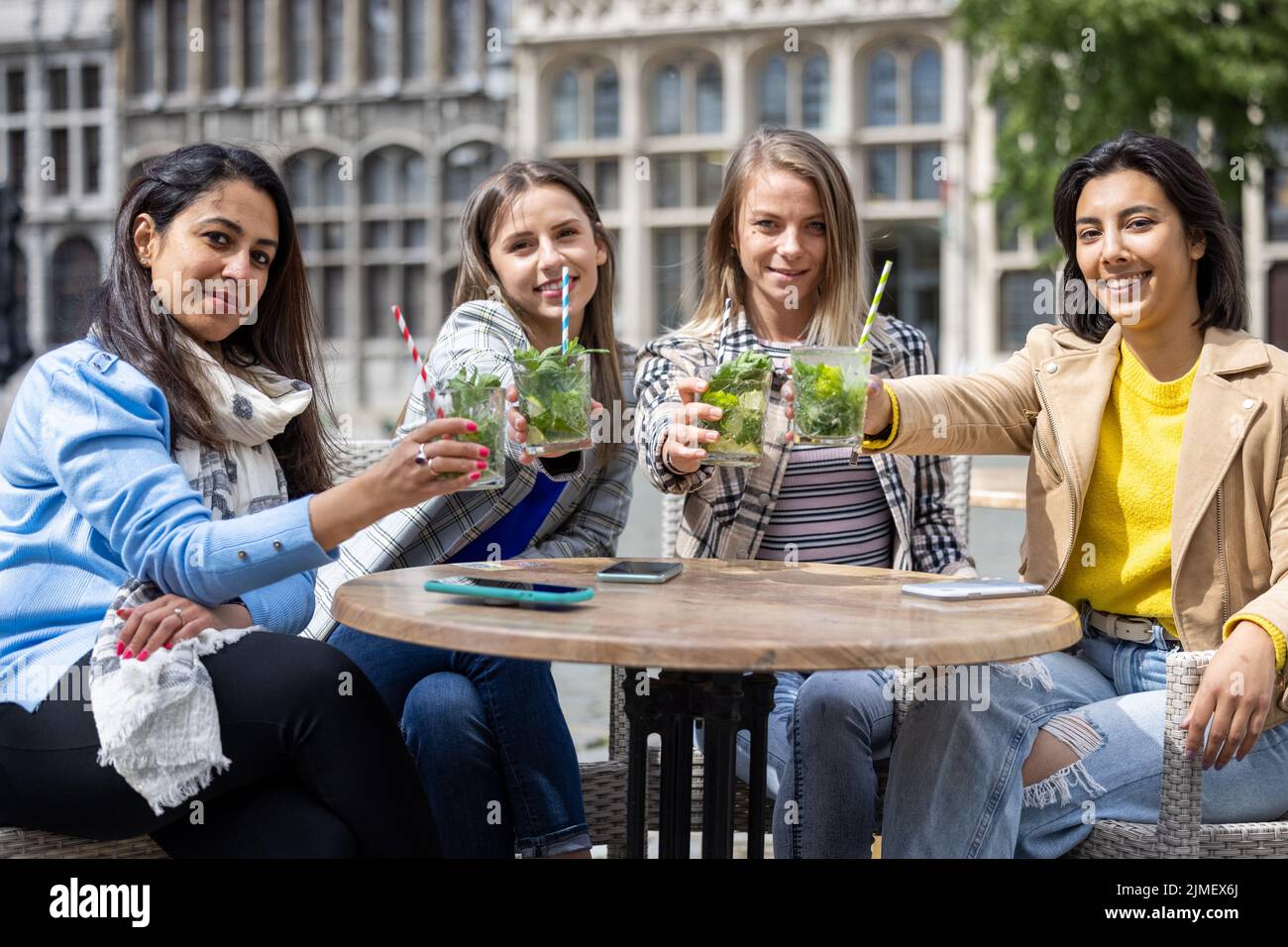 May 21, 2021, Antwerp, Belgium, Four attractive young woman of mixed race toasting with a cocktail outdoor in the city center af Stock Photo