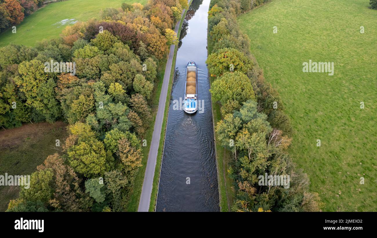 Aerial 4K Bird view shot with a drone of waterway with a barge or freight cargo ship sailing across the natural green orest and Stock Photo