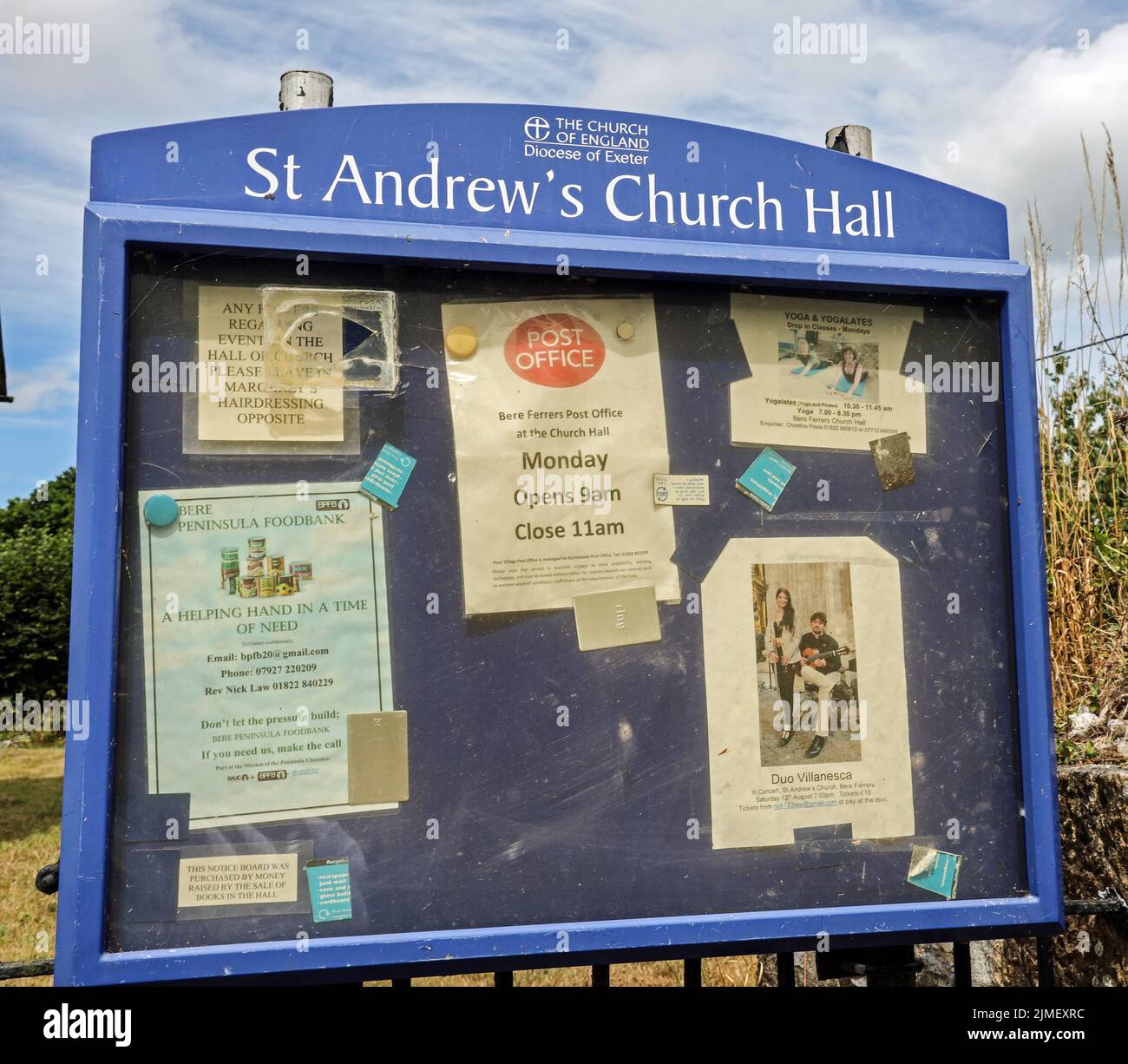 The noticeboard at St Andrew’s Church Hall at the little Devon Village of Bere Ferrers. A weekly post office service, Yoga and Help in a Time of Need Stock Photo
