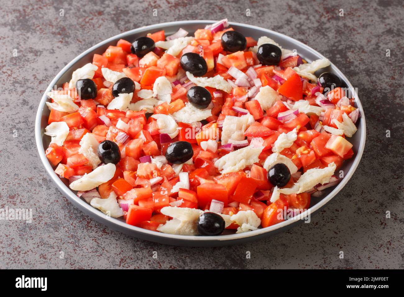 Spanish appetizer salad of salted cod, fresh tomatoes, onions and black olives close-up in a plate on the table. horizontal Stock Photo