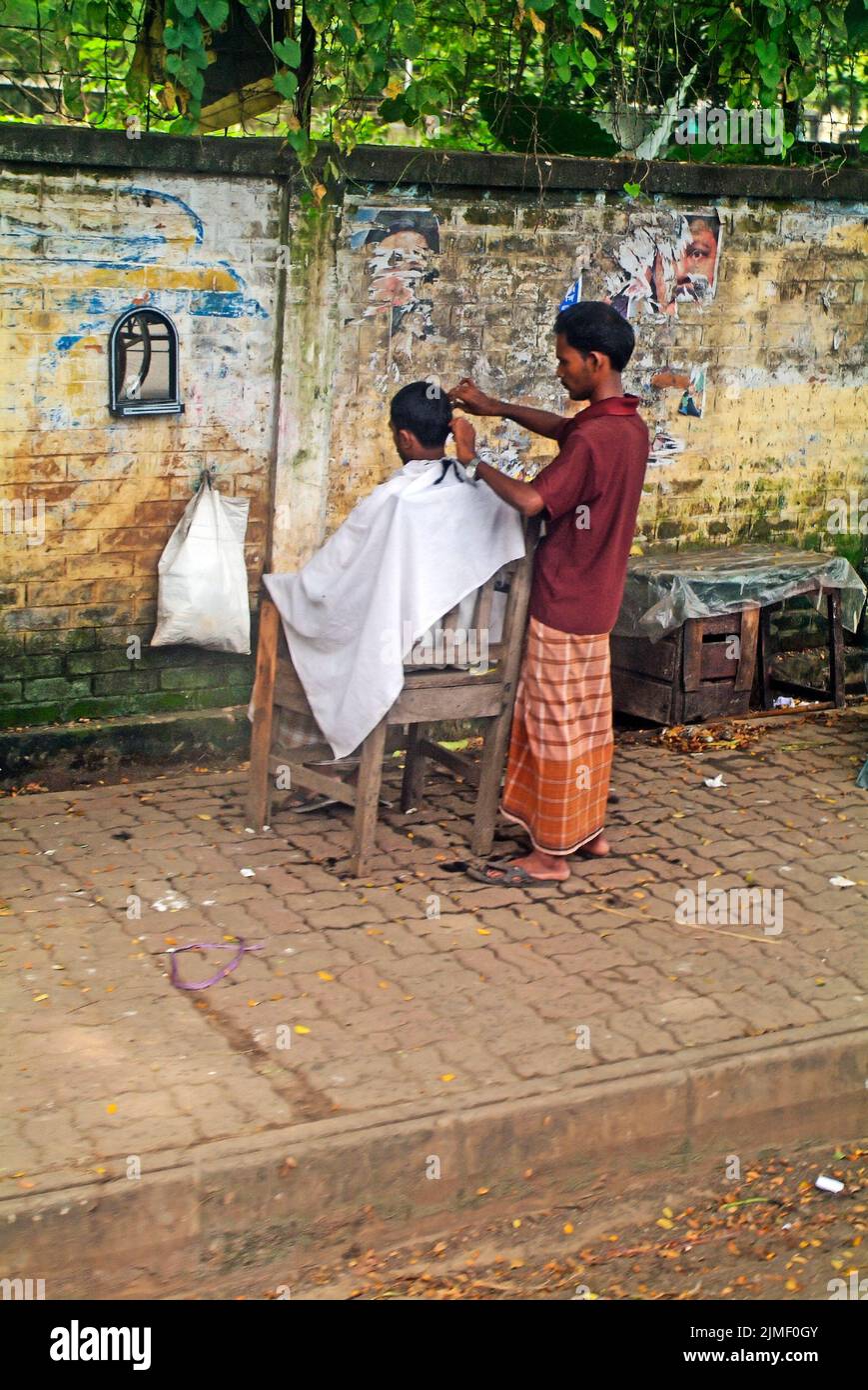 Dhaka, Bangladesh - September 17, 2007: Unidentified hairdresser cuts customers' hair on the sidewalk, an alternative for the poorer population Stock Photo