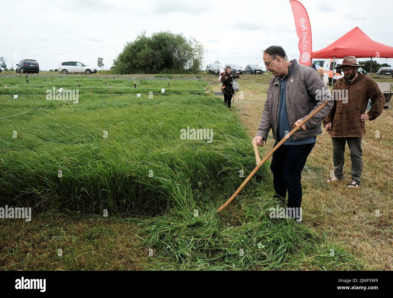 U.S. Ambassador to Lithuania Robert S. Gilchrist tries to use a scythe during Lithuanian mowing championship to cut down grass using scythes in Rupkalviai, Lithuania  August 6, 2022. REUTERS/Ints Kalnins Stock Photo