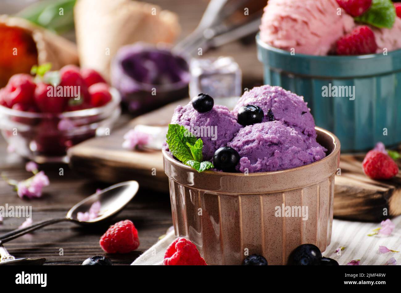 Blackberry icecream balls in clay bowls on wooden kitchen table with flowers and berries aside Stock Photo