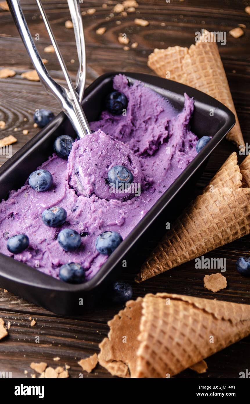 Blackberry icecream in tray with wafer cones aside on dark wooden kitchen table Stock Photo