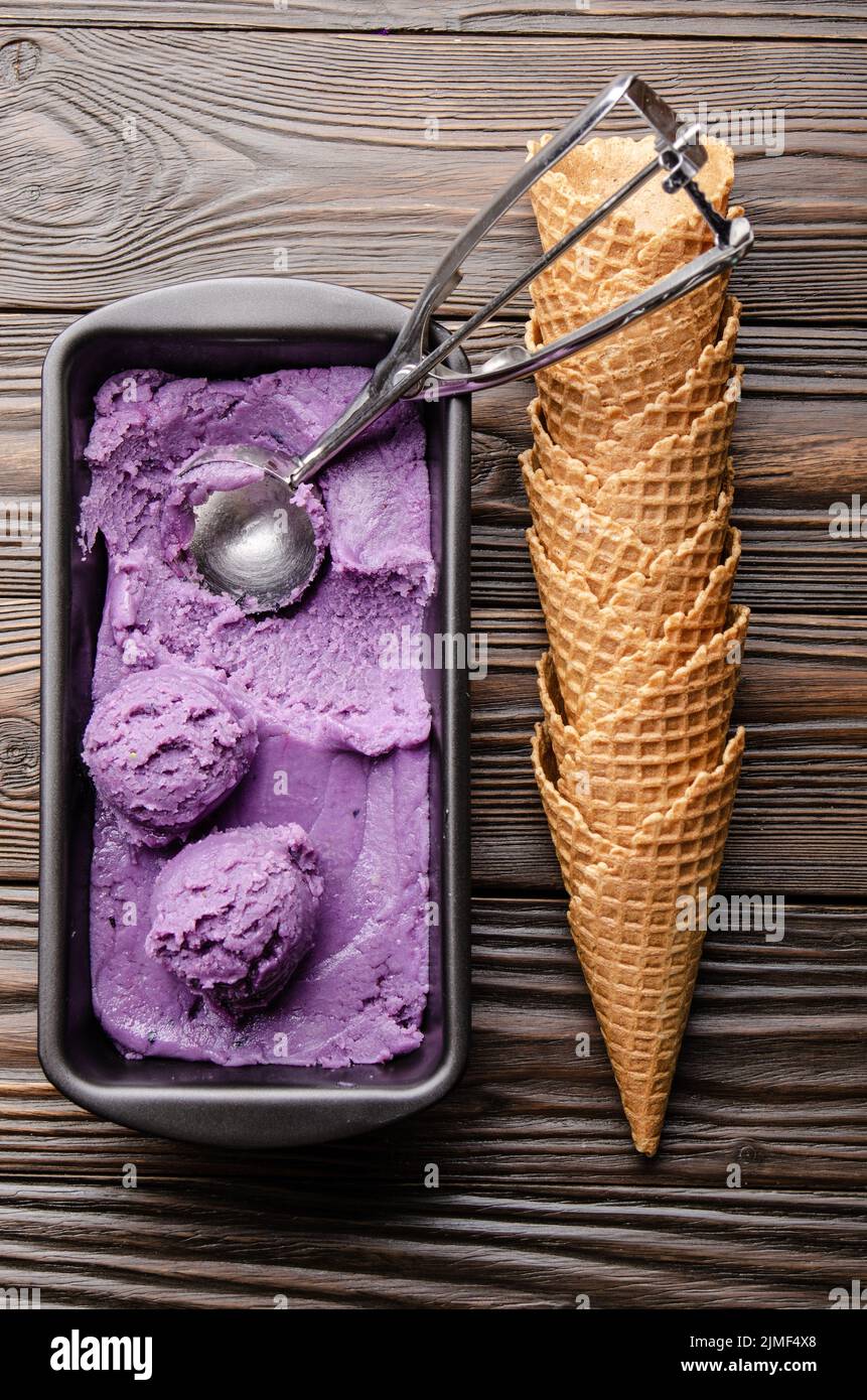 Flat lay view at blackberry icecream in tray with wafer cones aside on dark wooden kitchen table Stock Photo