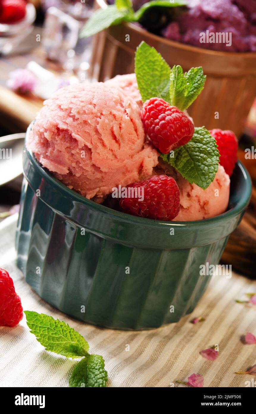 Pink Raspberry icecream balls in clay bowls on wooden kitchen table with berries and spoons aside Stock Photo