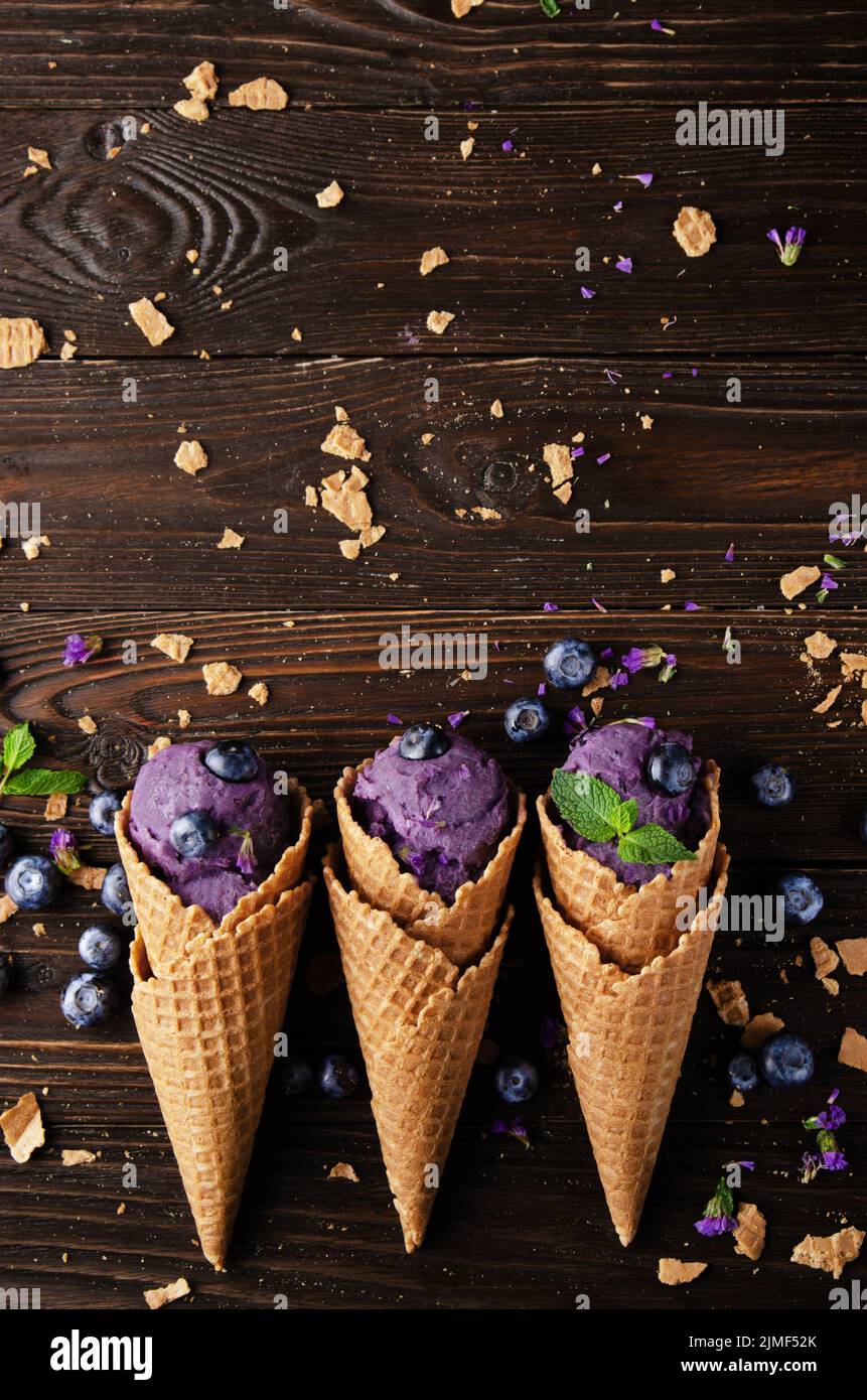 Flat lay view at wafer cones with blackberry icecream on wooden kitchen table Stock Photo